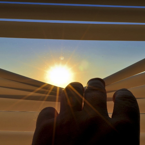image of hand pulling down window shades and the sun appearing from behind