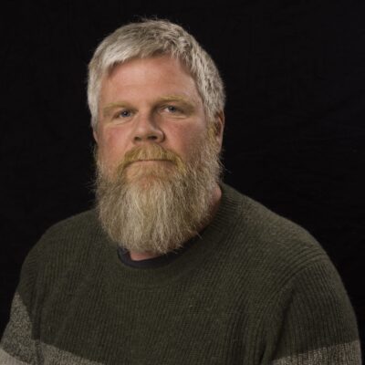 Image of Viggo Krüger, a male Norwegian music therapist with gray hair, a beard, and moustache, wearing a black and gray sweater
