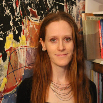 Music therapist, Laura Gillis. A woman with long, straight reddish hair, standing in front of a colorful backdrop.