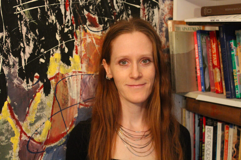 Music therapist, Laura Gillis. A woman with long, straight reddish hair, standing in front of a colorful backdrop.