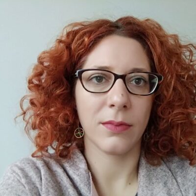 Dr. Potheini Vaiouli, who has medium length wavy red hair, wearing glasses and a gray sweater.