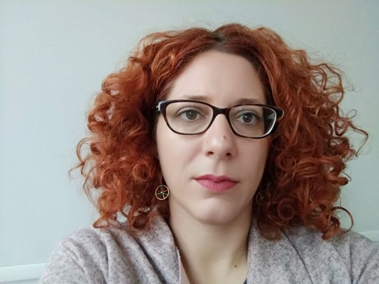 Dr. Potheini Vaiouli, who has medium length wavy red hair, wearing glasses and a gray sweater.