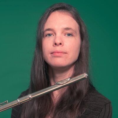 Music therapist, Hilary Davies, who has long, straight, brown hair, and is holding a flute in front of a green background