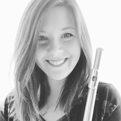 Music therapist, Krystine Smith, who has straight, light-colored, shoulder-length hair, and is wearing a floral top and holding a flute