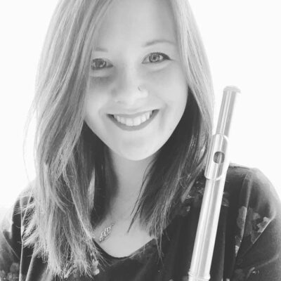 Music therapist, Krystine Smith, who has straight, light-colored, shoulder-length hair, and is wearing a floral top and holding a flute