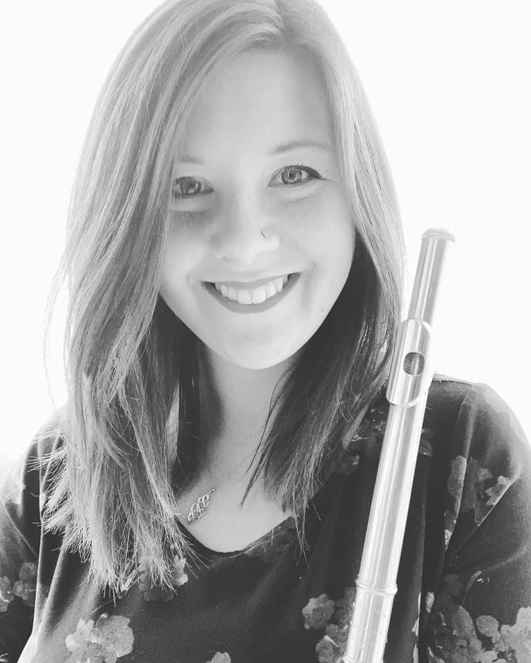 Music therapist, Krystine Smith, who has straight, light-colored, shoulder-length hair, and is wearing a floral top and holding a flute